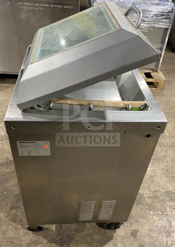 Multivac stainless steel chamber vacuum packing machine, shown with open lid. Features durable construction and mobility wheels.