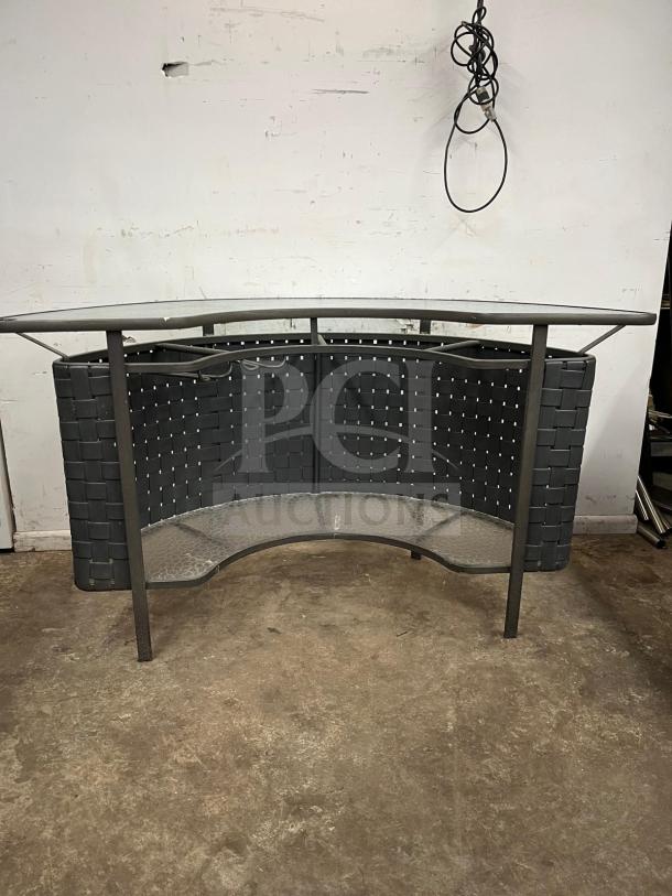 Curved outdoor bar with woven design, metal frame, and glass shelf. Good condition suitable for patio or garden use.