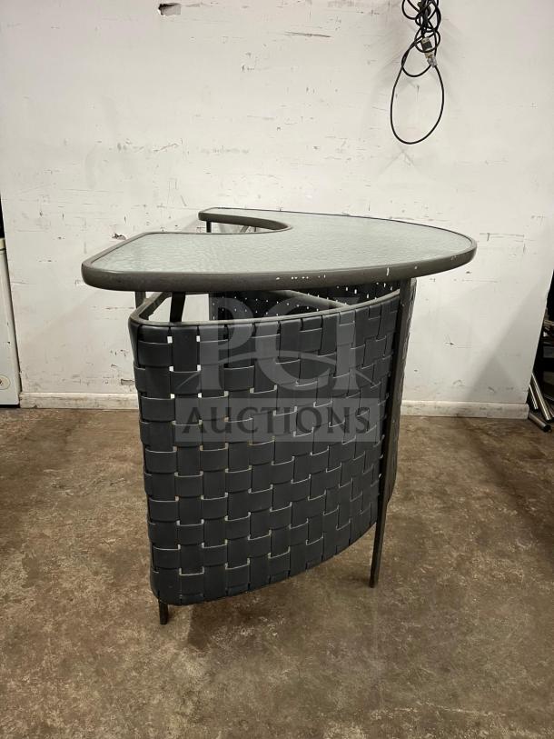 Curved outdoor bar with glass top, dark woven design, metal frame. Appears in good condition, ideal for patio use.