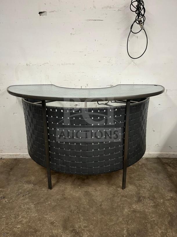 Curved outdoor bar with glass top, black woven detailing, and metal frame. In good condition, ideal for patio use.