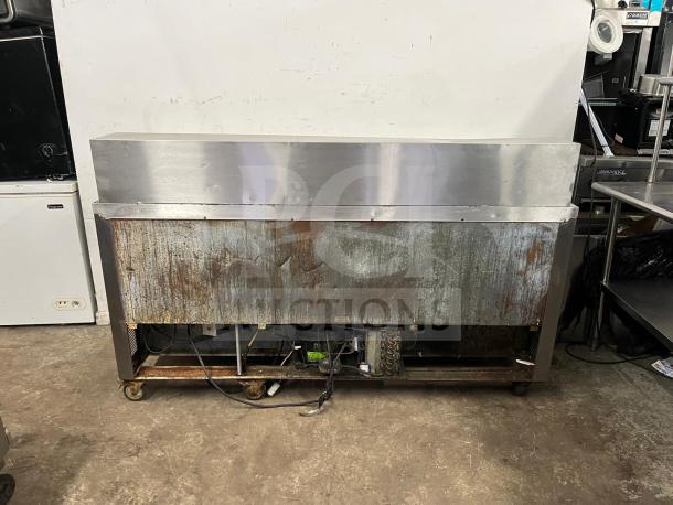 LEADER NSFM72 72" 3-door refrigerated prep table in used condition, showing rust on metal exterior, with visible wheels and electrical components.