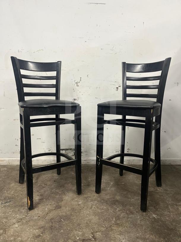 Pair of bar stools with black sandthru finish and faux leather seats. Some wear visible on the legs.