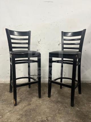Pair of bar stools with black sandthru finish and faux leather seats. Some wear visible on the legs.