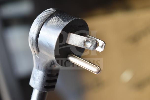 Close-up of a black power plug for the True TVM-48SL-HC commercial refrigerator, 115 volts, showing prongs and cable housing.