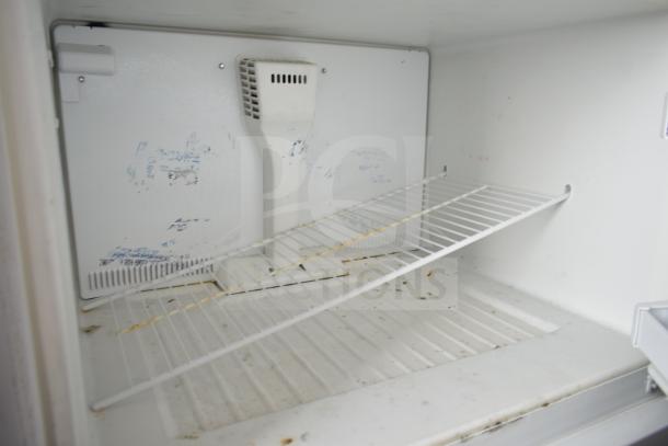 Whirlpool W1TXNMFWQ00 cooler with freezer, interior view. Features wire shelf, signs of wear, functional for storage.
