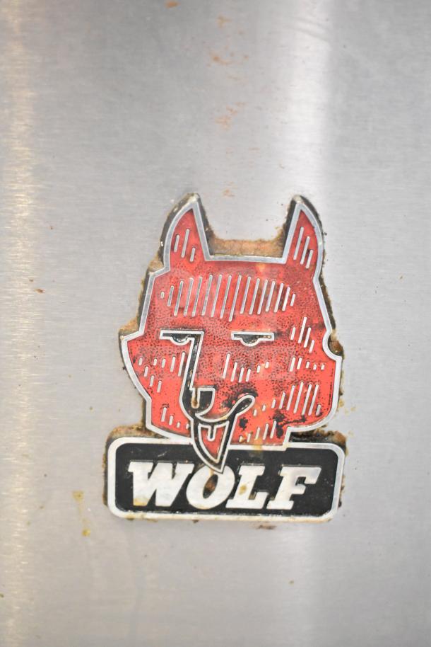 Wolf CHSSR-6-29 commercial range logo, featuring a red wolf design, on stainless steel surface.