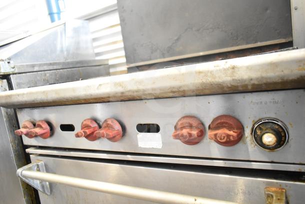 Wolf CHSSR-6-29 commercial gas range, 6 burners, oven, metal backsplash, visible wear, labeled control knobs.