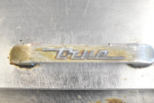 True TSSU-60-24M-B prep table handle with brand logo, showing wear. Stainless steel surface visible.
