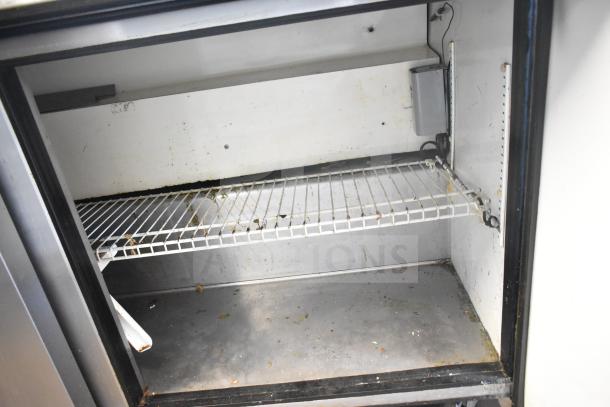 True TSSU-60-24M-B commercial sandwich salad prep table interior, showing a wire shelf. Some signs of wear, needs cleaning.