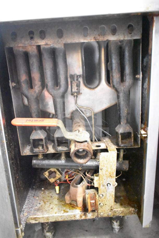 Commercial gas-powered deep fat fryer, interior view showing gas burners and connections, moderate wear visible.