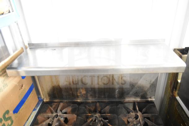 Imperial commercial gas-powered 6 burner range with oven, over shelf, and back splash. Shows signs of use.