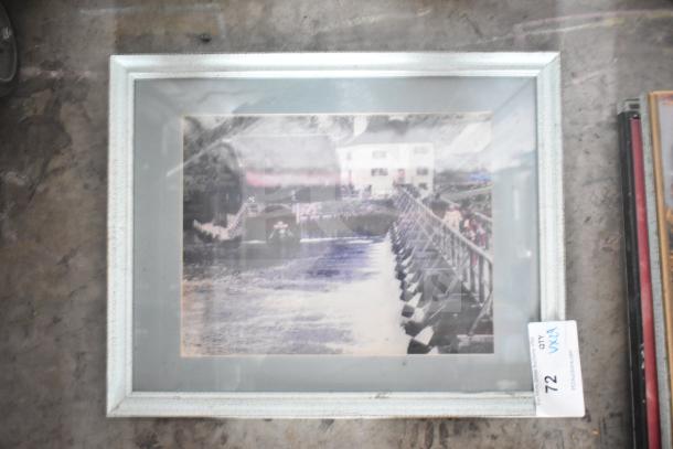 Framed picture of a bridge and buildings, vintage look. Light-colored frame, slight wear. Auction tag visible.