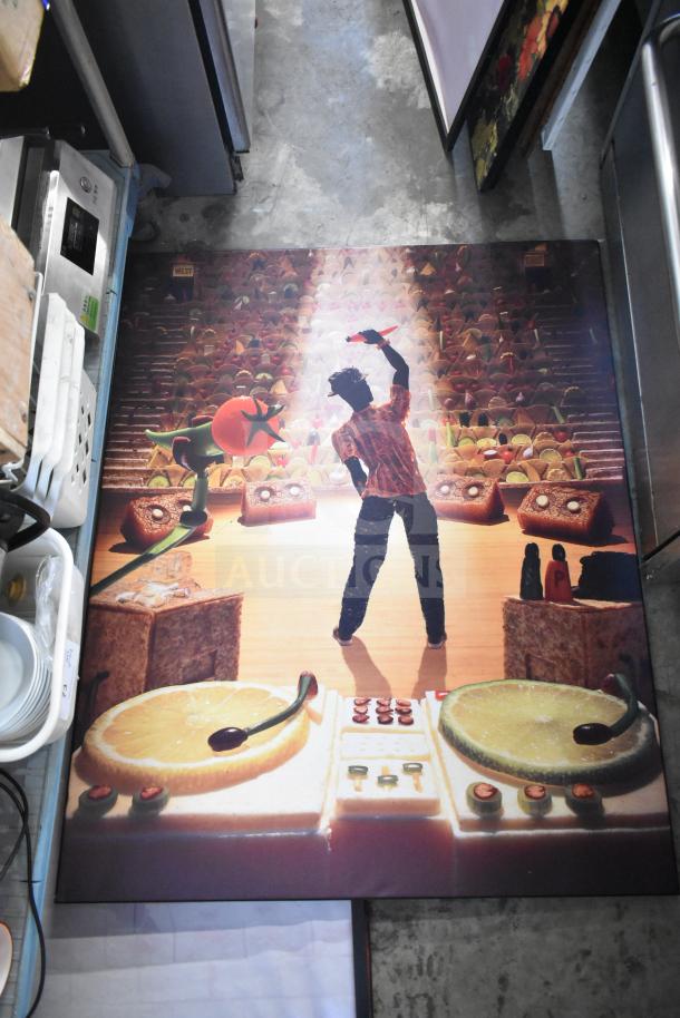 Framed picture featuring a surreal scene with decorative food elements and a figure on stage. Part of a lot of 29 varied framed artworks.