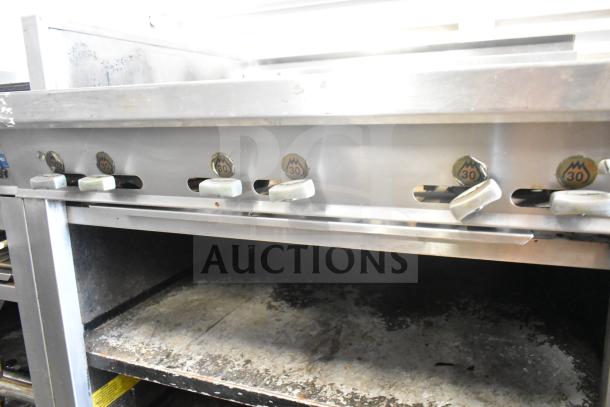 Montague UF-36R gas range with 6 burners, left side charbroiler, under shelves, and commercial casters, in used condition.