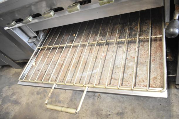 Montague UF-36R commercial range with 6 burners, left side charbroiler, under shelves, on casters; visible used condition.