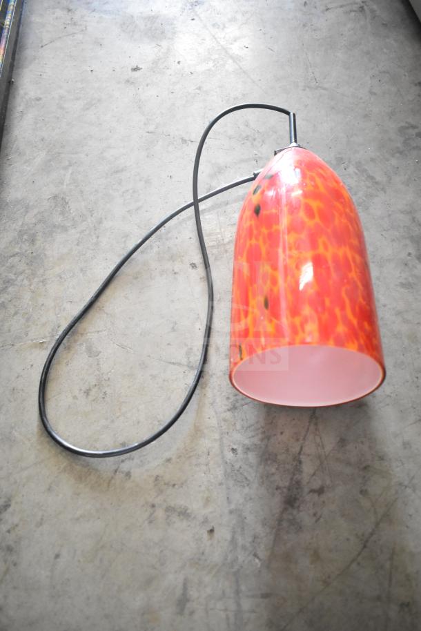 Orange glass pendant light with a black cord on a gray concrete floor. Features a marbled design.