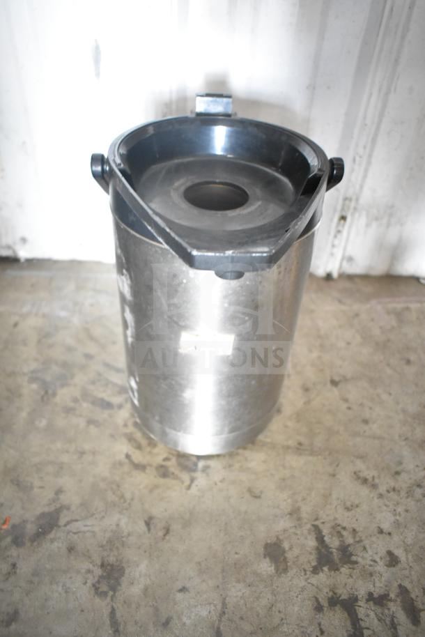 Metal air pot with black lid and secure latches, resting on a concrete floor, light scratches visible.