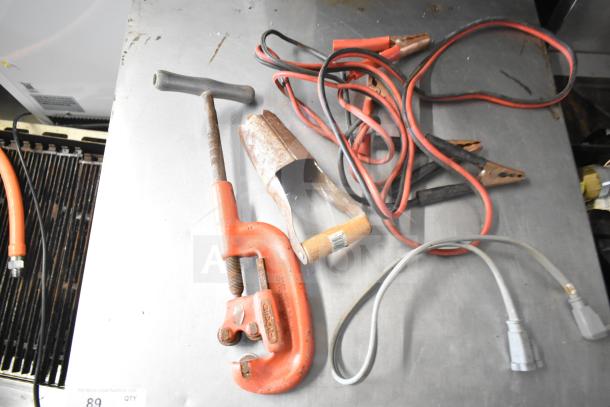 Various items on a metal surface, including a Ridgid clamp, jumper cables, and assorted tools. Used condition.