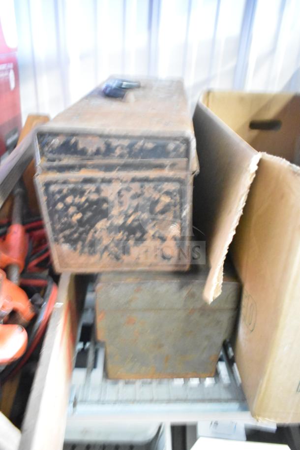 Lot of items including a rusty metal toolbox, jumper cables, and a clamp, all showing signs of wear and use.