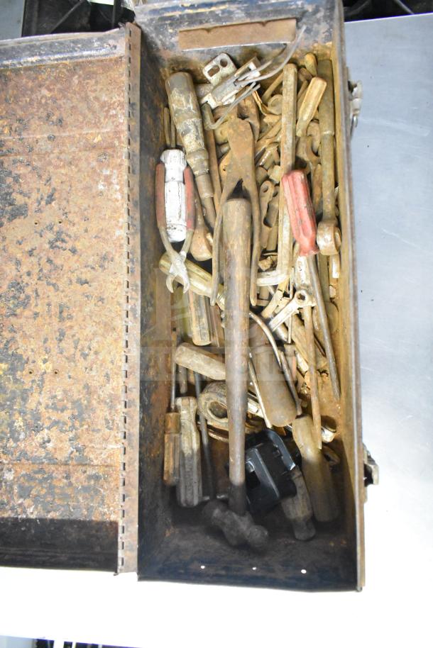 Rustic toolbox filled with assorted tools, clamps, and jumper cables. Visible rust, various sizes, conditions vary.