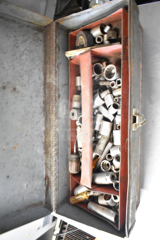 Open metal toolbox with assorted sockets and hand tools, showing signs of rust and wear.