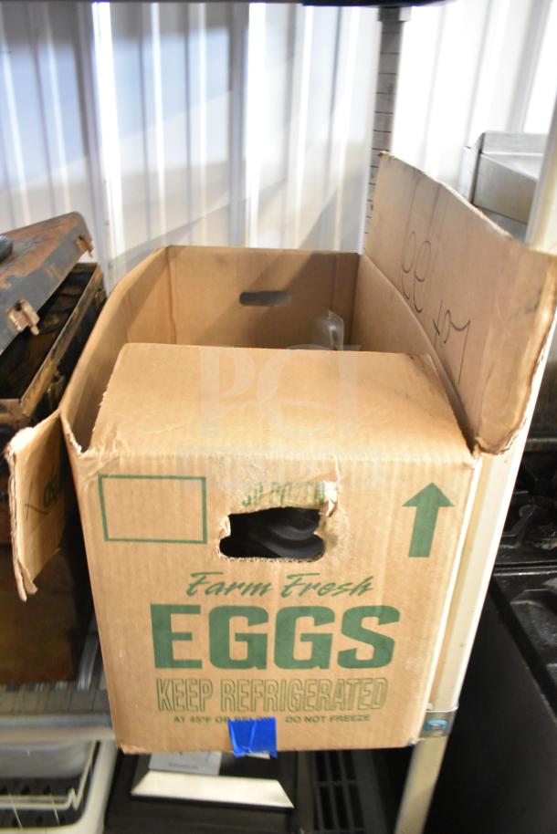 Cardboard box labeled "Farm Fresh Eggs" containing miscellaneous items like tools, clamp, and toolbox, in used condition.