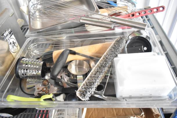 Lot of kitchen items including stainless steel bins, whisks, grater, utensils, cutting board, and baking sheets in used condition.
