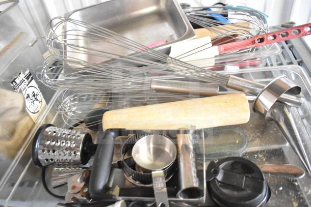 Lot of kitchen items including stainless steel drop-in bins, whisks, grater, measuring cups, and cutting board.