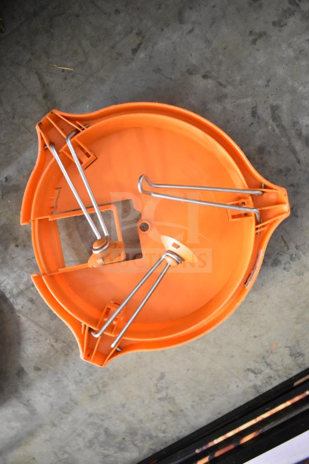 Orange countertop vegetable cutter, round shape, with metal blades, seen from top view. Appears in good condition.
