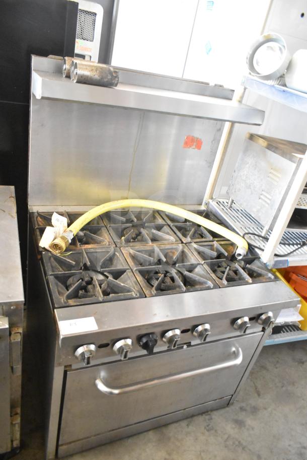 Commercial gas-powered 6 burner range with oven, over shelf, and backsplash. Stainless steel, used condition, includes gas hose.