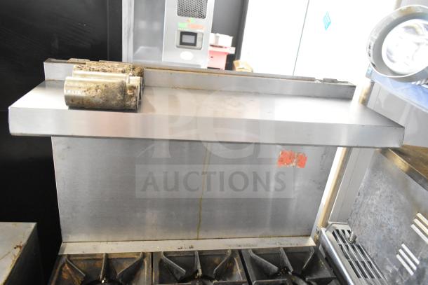 Commercial gas-powered 6 burner range with oven, featuring overshelf and backsplash. Shows signs of use.