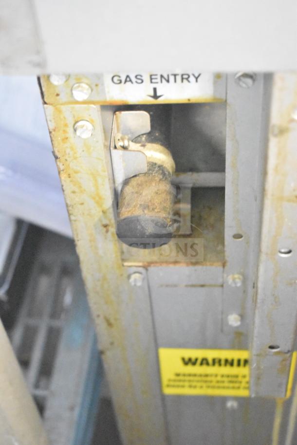 Rusty gas entry point on a commercial gas-powered 6-burner range with visible warning label.