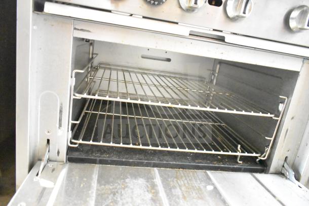 Commercial gas-powered 6 burner range with oven, over shelf, and backsplash, metal finish, visible wear, interior oven racks shown.