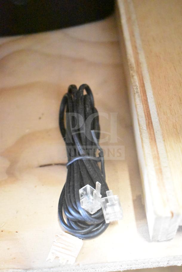 A coiled black cable with clear connectors sits on a wooden surface.