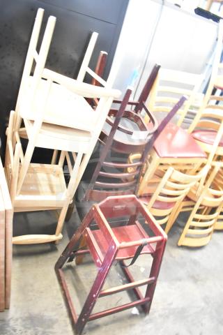 Stacked wooden and metal chairs, including a high chair and dining chairs, in good condition. Auction lot of seven items.