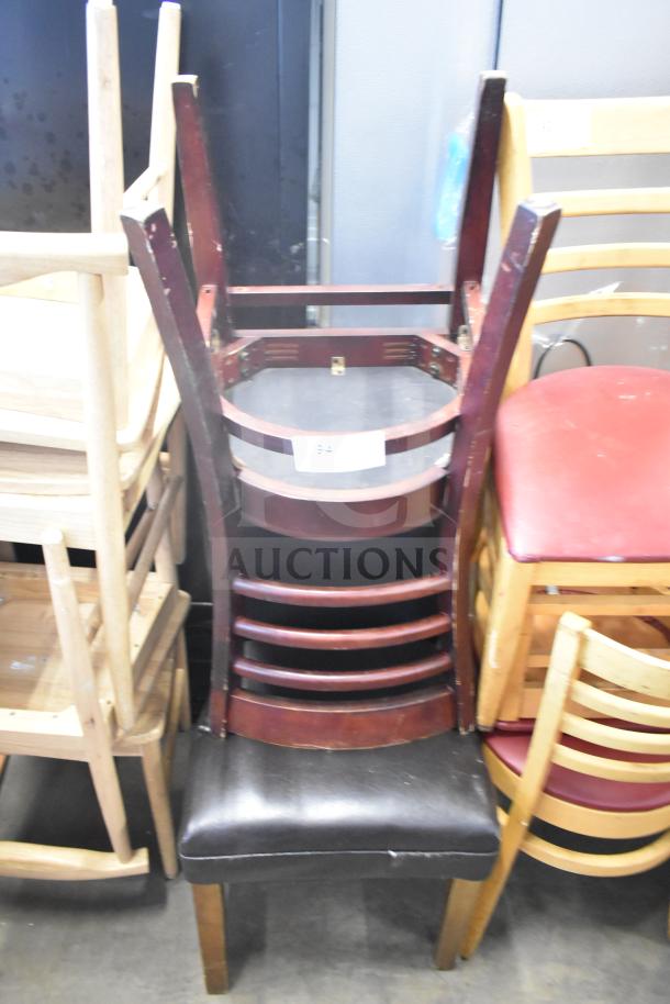 Seven assorted chairs stacked, including a high chair and dining chairs. Mixed wood and upholstery. Condition varies.