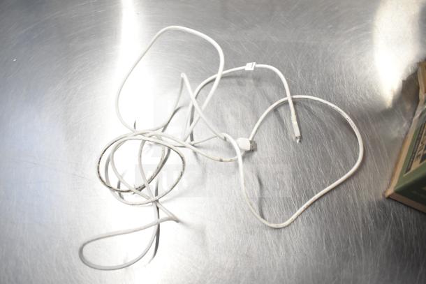 A tangled white USB cable on a metallic surface, showing signs of wear with black marks. No visible tags or labels.