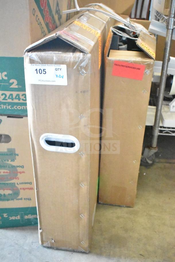 Two cardboard boxes labeled for auction, containing a camera and a 32" monitor. Box shows PCI Auctions label with item number 105.