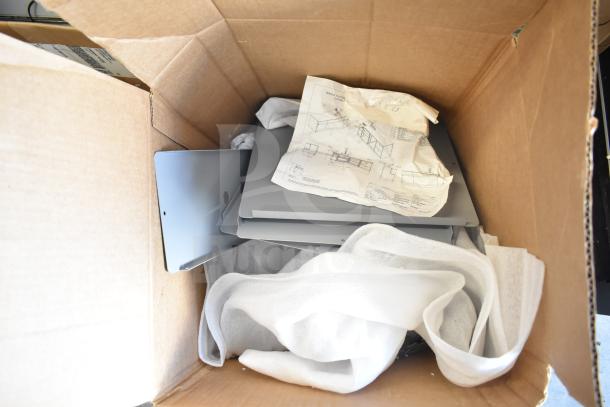 Cardboard box containing various metal pieces and an instruction sheet, possibly for assembly. Items appear new.