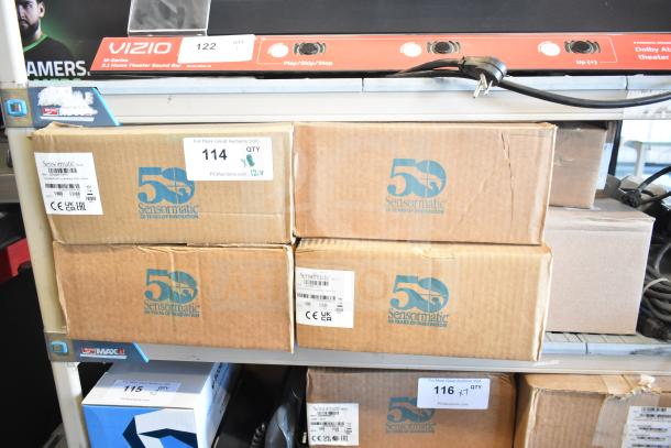 Boxes labeled "Sensormatic 50 Years of Innovation" with auction tags, containing electronics like label deactivators and cameras.