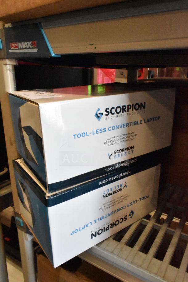 Two Scorpion 720029-B tool-less convertible laptop security devices in boxes, on storage shelves.