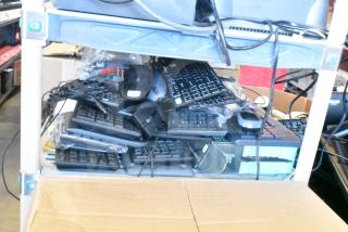 Lot of various computer peripherals including keyboards and mice, stacked on shelves, assorted brands and models.