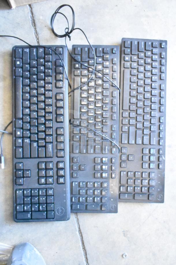 Lot of three black wired computer keyboards on concrete floor, showing various layouts and light wear.
