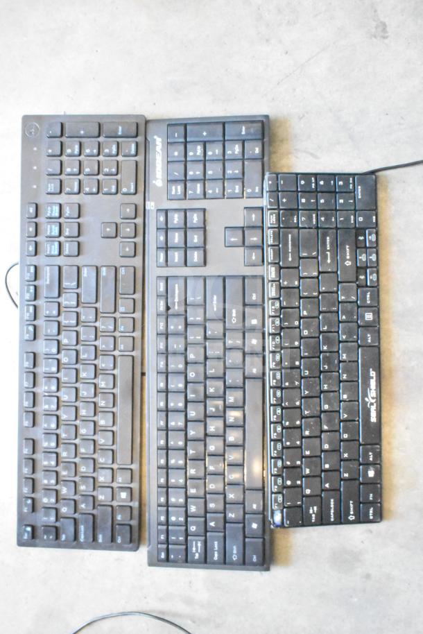 Lot of three black computer keyboards with visible brands: Anker, Seal Shield, and another with a logo.