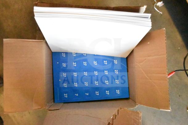 Open cardboard box containing blue sheets with the number 27 and a stack of blank white papers. No visible electronic items.