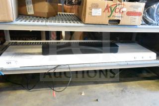 Bose sound bar on a shelf, black, in used condition, power cord visible, lot label QTY 121 displayed.