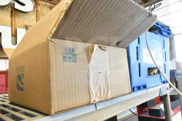 Open cardboard box with Sensormatic ZBAMB9012 label deactivator pad and computer keyboards, on a shelf.