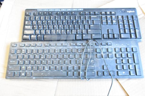 Two wired computer keyboards, brands Dell and Logitech. Both show signs of use, placed on a cardboard surface.