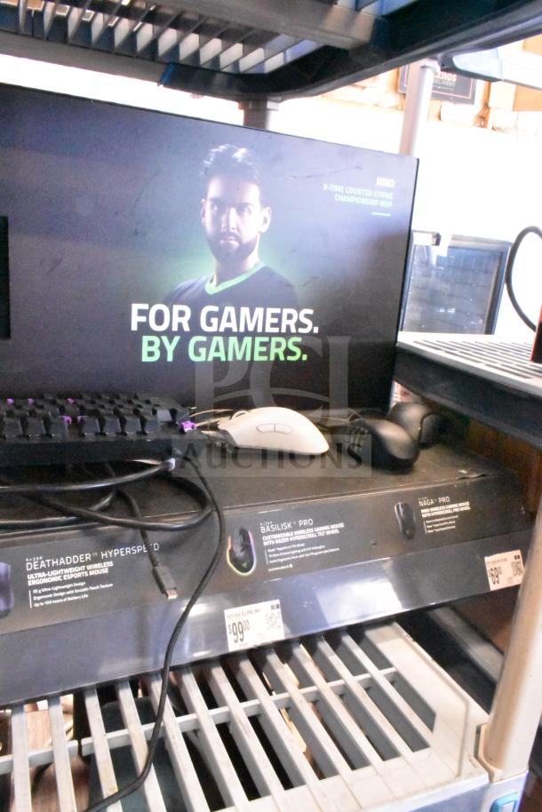 Gaming store display with headphones, keyboard, and computer mice. Features promotional poster and price tags for gaming accessories.