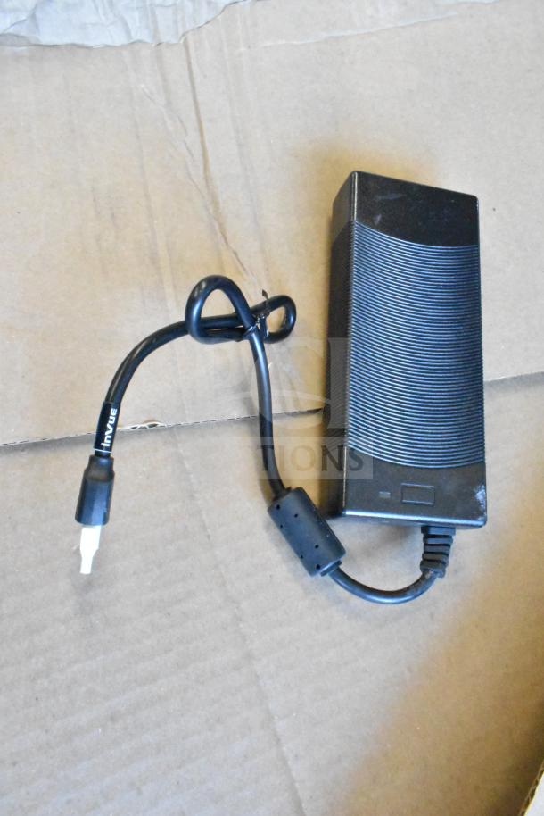 Black rectangular device with attached cable featuring a visible "InVue" label. Placed on cardboard surface.